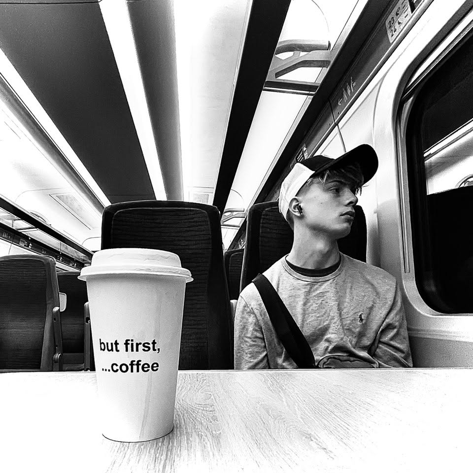 Black and white photo of a coffee cup reading but first, ...coffee on a train table
